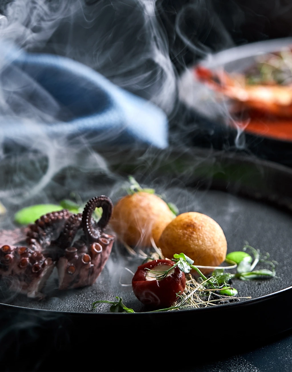 Mains de la cheffe dressant une petite assiette en céramique près d’un feu de bois